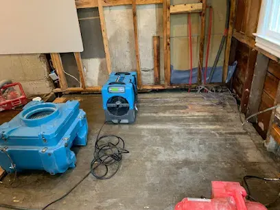 Air movers drying a stripped floor and open wall framing after water damage